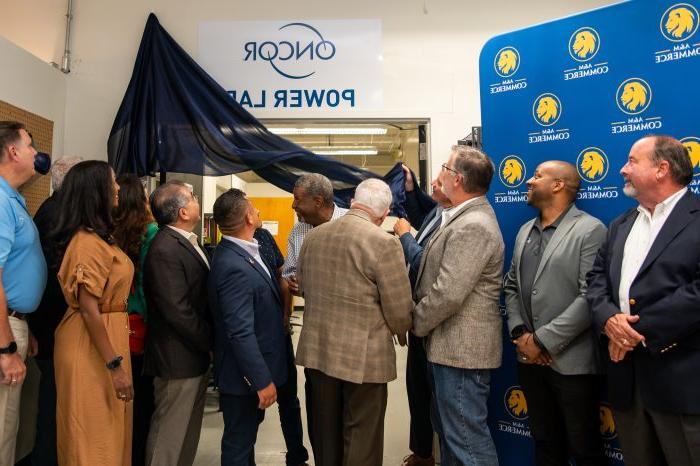 People look above doorway as curtain is pulled down to reveal "Oncor Power Lab" sign.