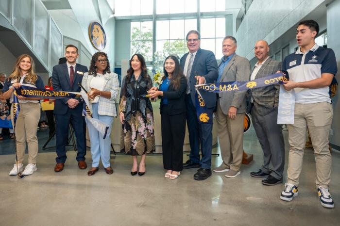 Eight people line up and hold a blue ribbon in front of them, which was cut in the middle.